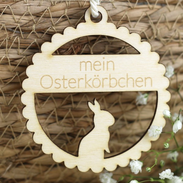 Osteranhänger mit Hase und Schrift an Körbchen mit Blumen