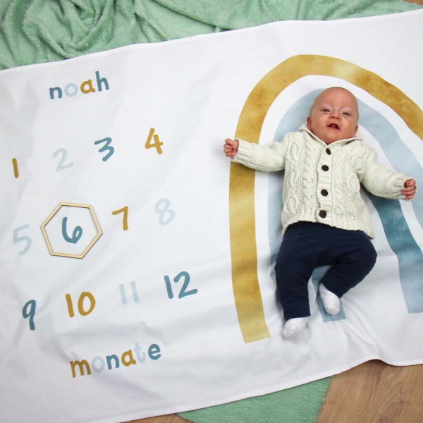 Meilensteindecke für das erste Lebensjahr mit buntem Regenbogenmuster, Monatskalender und personalisiertem Namen über diesem, hier mit Sechseckkranz zur Markierung des Alters